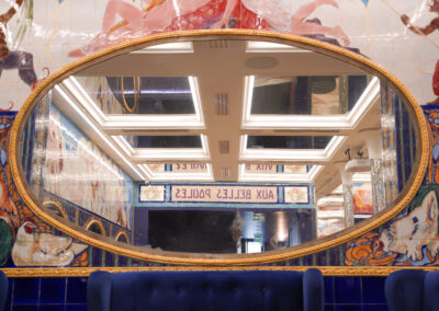 Grand miroir ovale doré gravé Aux Belles Poules au-dessus d'une banquette de velours