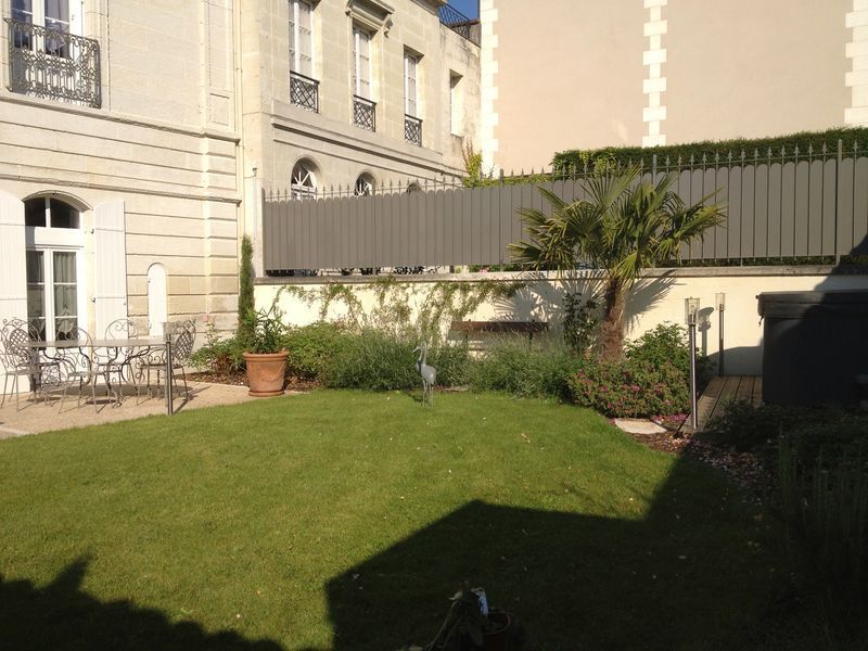 Jardin de ville avec pelouse, terrasse et plantations près d'une demeure en pierre