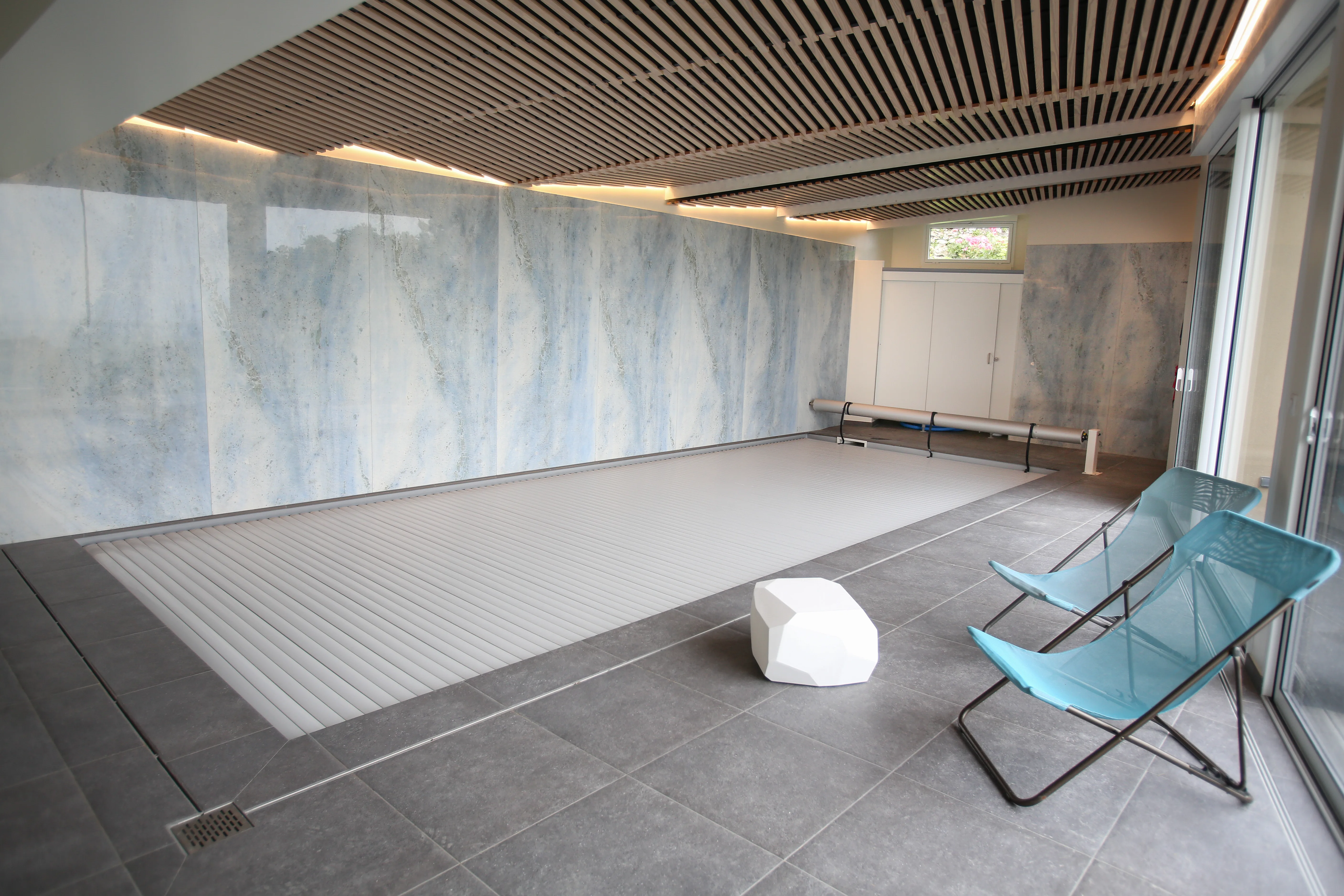 Espace piscine intérieure avec plafond lames de bois et murs effet marbre