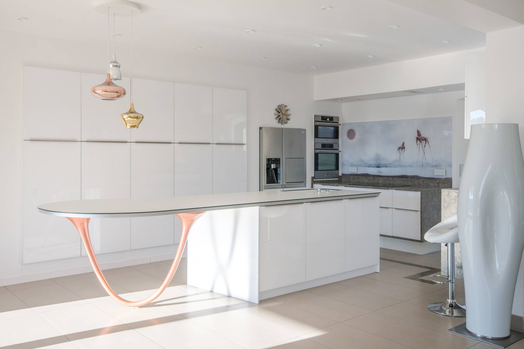 Cuisine d'architecte blanche avec îlot sculptural et suspensions cuivre, réalisée par Cuisines Passions