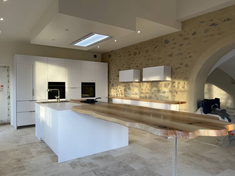 Cuisine blanche contemporaine avec bar en bois massif à bord vivant, adossée à un mur de pierres provençal