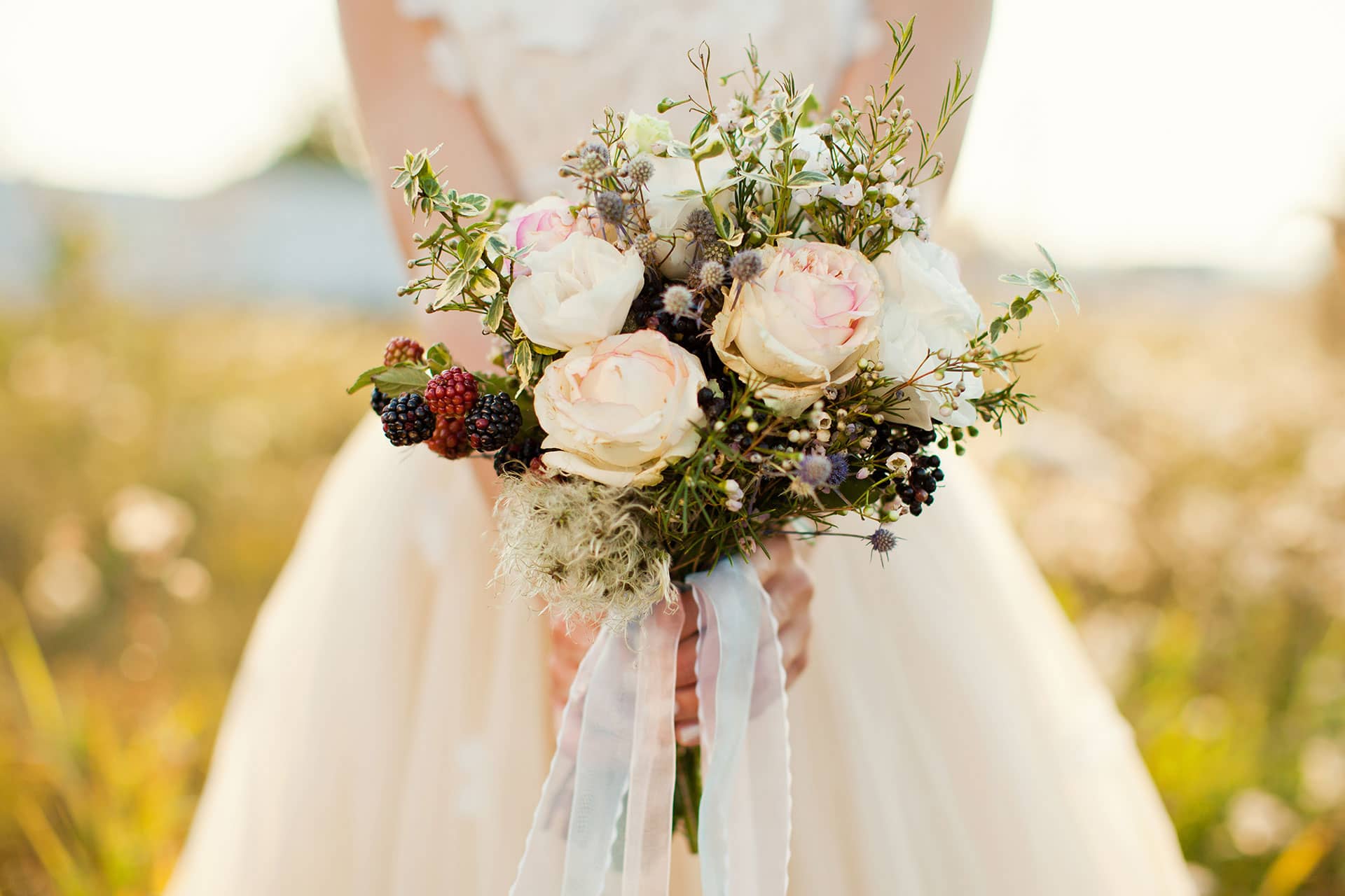 Bouquet de mariée champêtre, fleurs et baies, dans un champ baigné de lumière