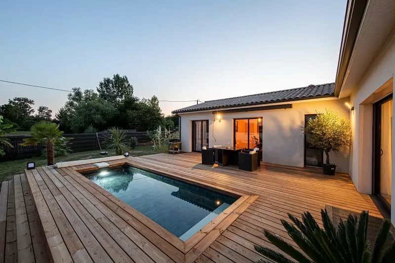 Piscine enterrée posée par EAUSOL au crépuscule, terrasse bois et maison du Gers