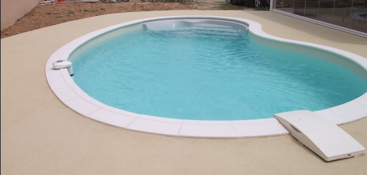 Piscine forme libre à l'eau turquoise sur plage de béton sablé