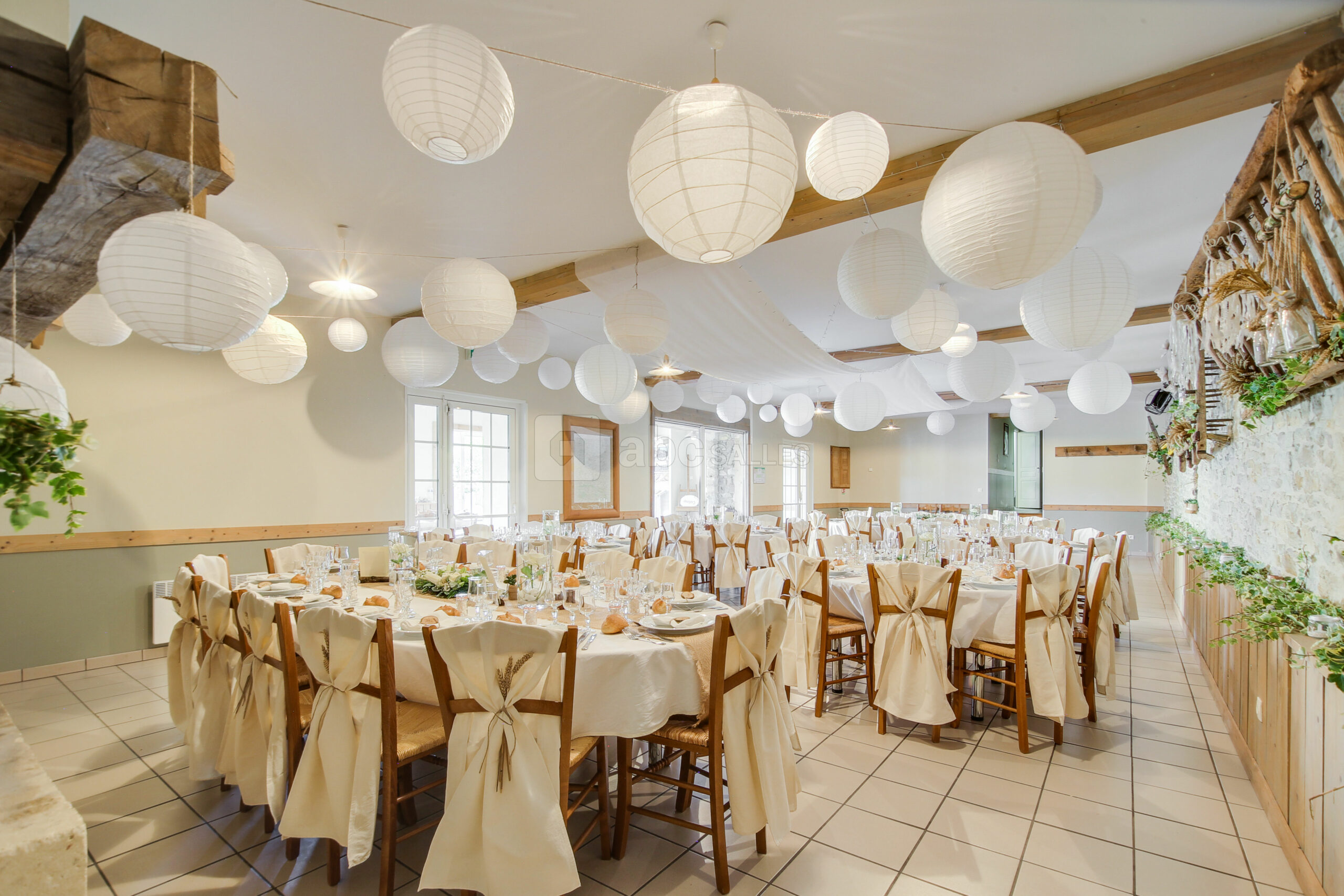 La salle de réception du Gîte de la Cour dressée pour un repas, longues tablées sous des lampions en papier.