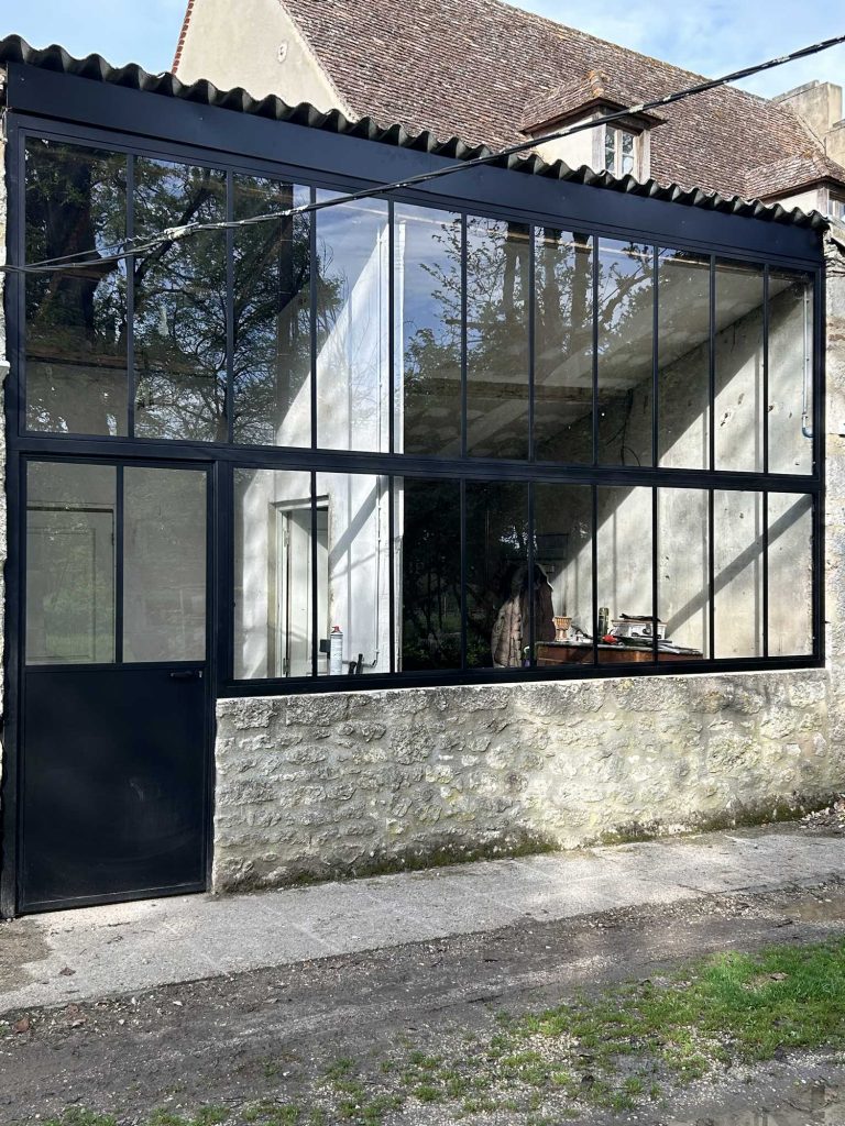 Verrière atelier en acier noir réalisée par JC Industriel à Bergerac, posée sur un mur en pierre