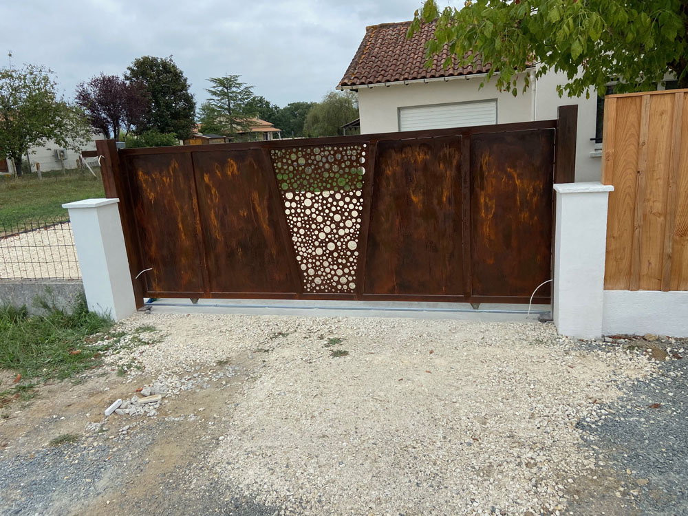 Portail coulissant en acier corten avec motif découpé, posé entre deux piliers