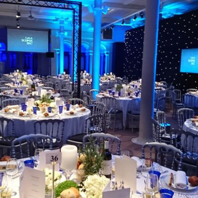 Gala : tables rondes dressées sous les colonnes, fond étoilé bleu nuit