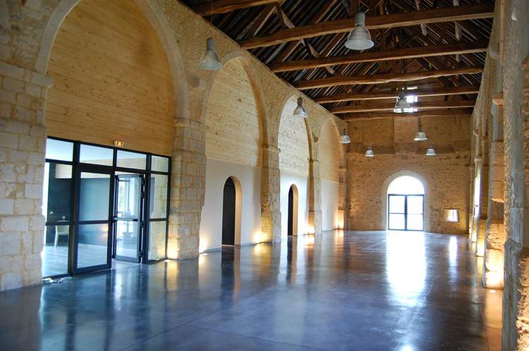 Interieur de la grange du XIVe siecle : charpente en bois, arches de pierre et sols polis baignes de lumiere