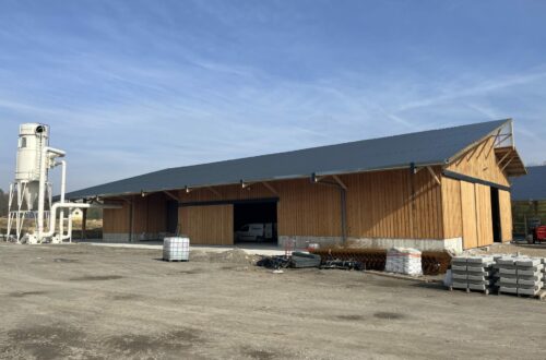 Grand bâtiment agricole en bois à toiture sombre, en cours d'aménagement sur son terrain