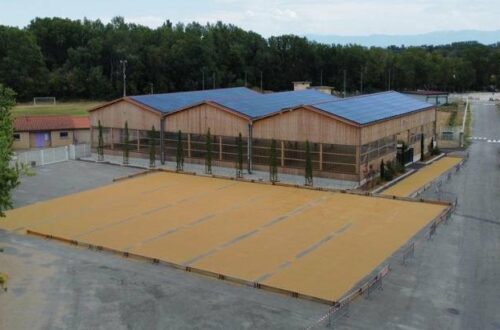 Complexe sportif en bois vu du ciel, toiture couverte de panneaux photovoltaïques et terrains extérieurs