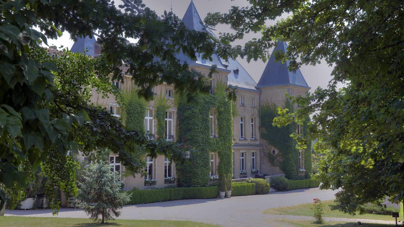 Le Château d'Adoménil, façade du 18e siècle aux tourelles d'ardoise, voilée de lierre et entourée d'arbres du parc