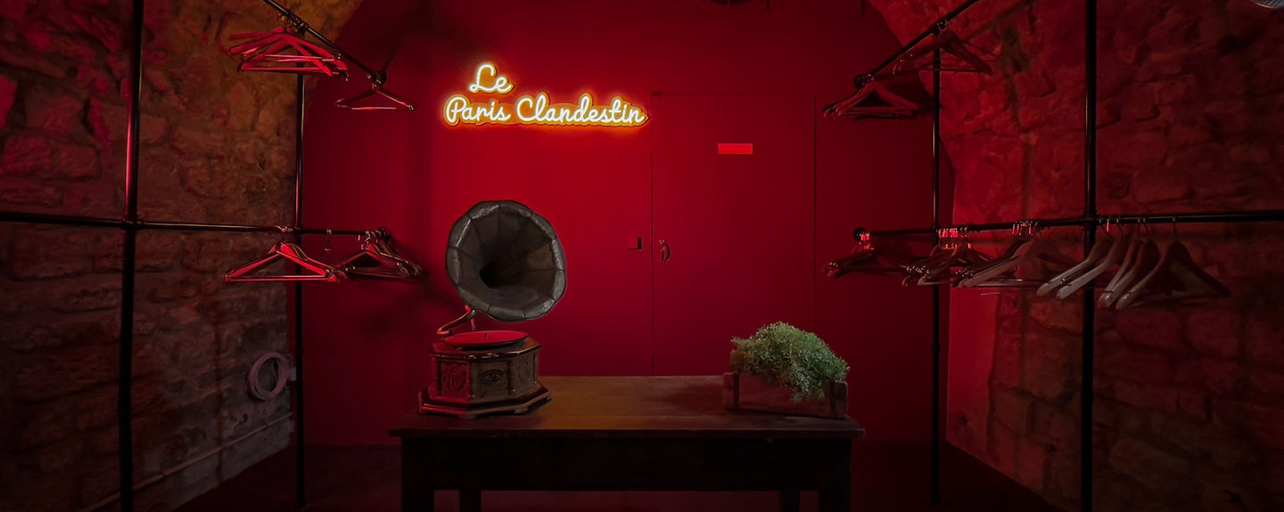 Le vestiaire rouge du Paris Clandestin, enseigne néon et gramophone ancien sur fond de pierre