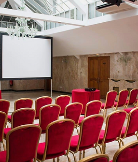 Salon configuré en conférence, écran et chaises rouges.