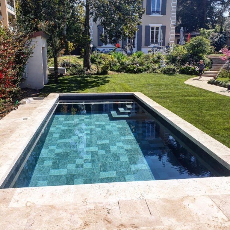 Piscine à revêtement mosaïque verte devant une demeure ancienne, jardin fleuri.