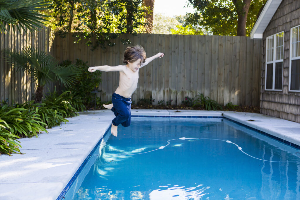 Enfant sautant dans une piscine au fond d'un jardin
