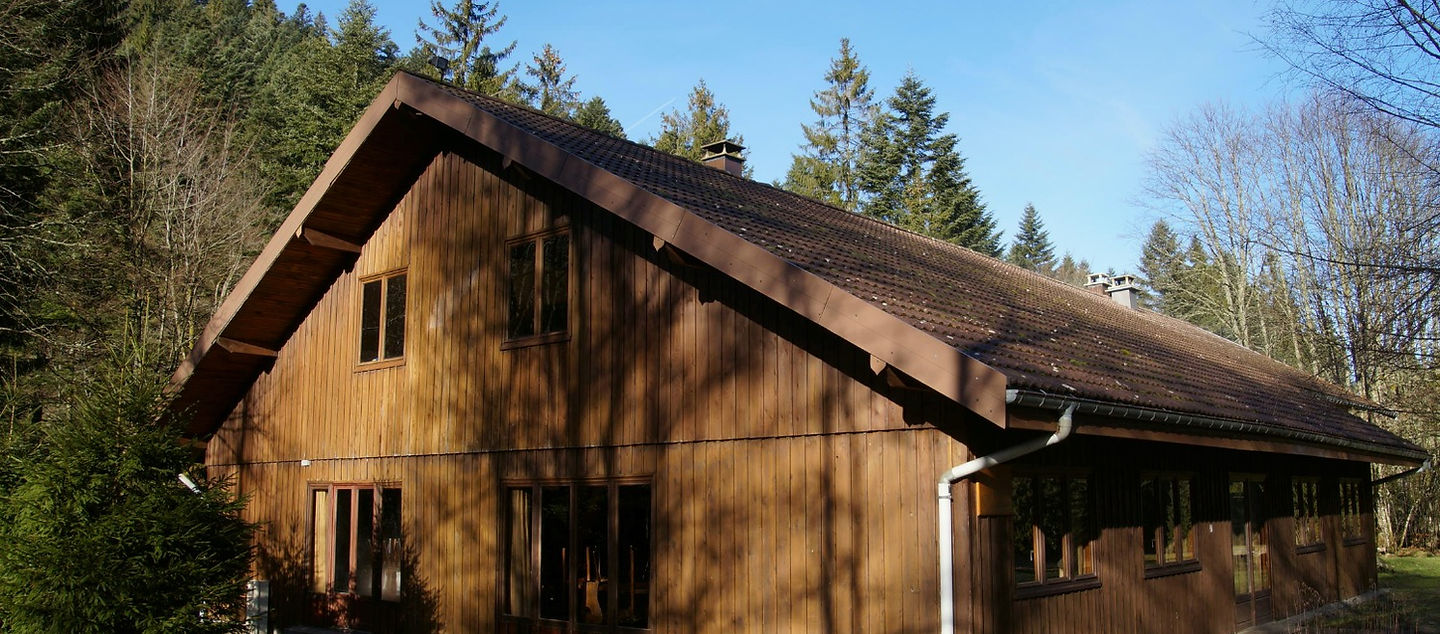 Le chalet en bois de la Salle Le Cellet sous un ciel bleu, lisière de la forêt vosgienne
