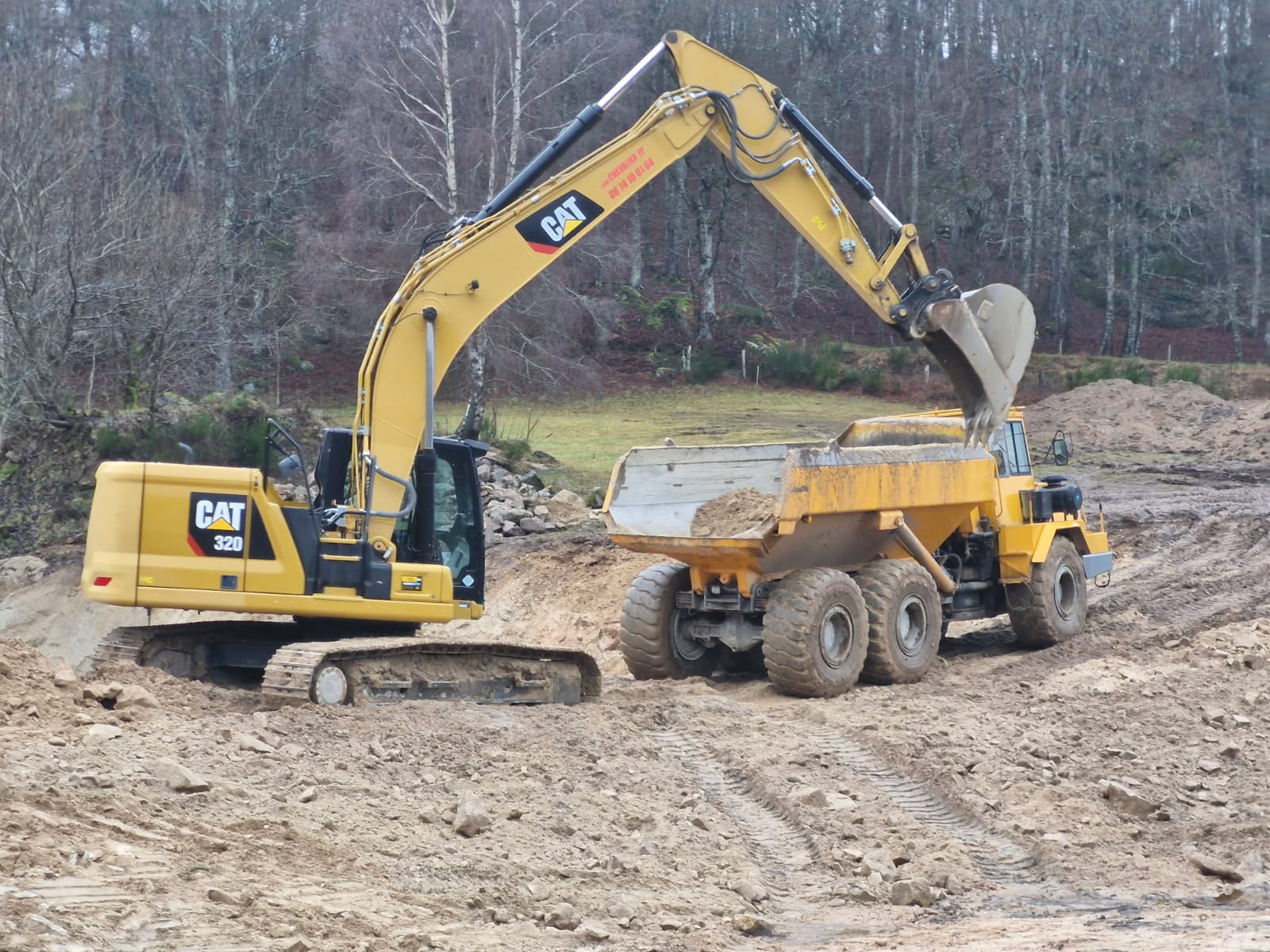 Pelle CAT 320 chargeant un tombereau sur un chantier de terrassement en Lozère