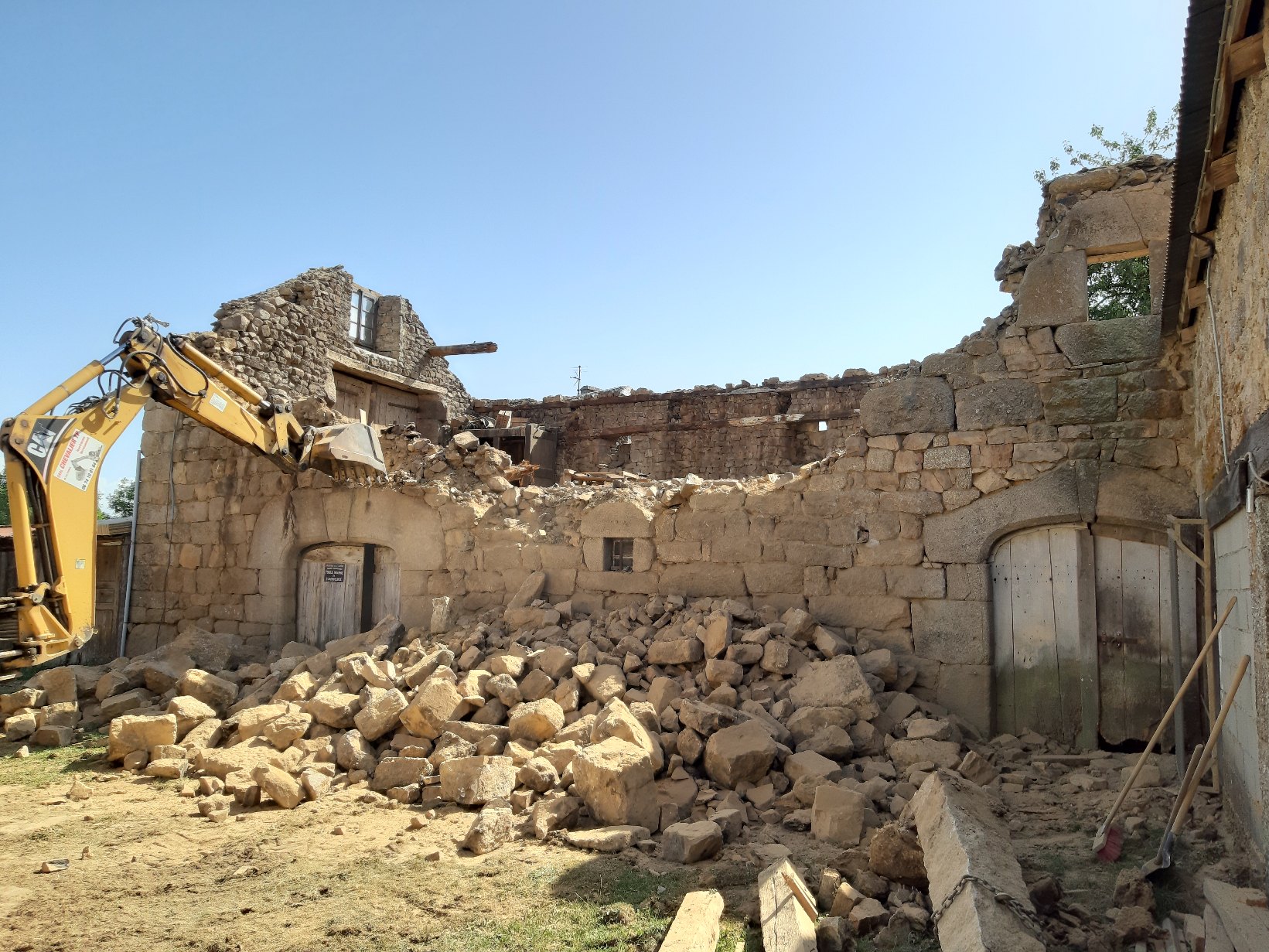 Démolition d'une grange en pierre par une pelle CAT, ciel bleu