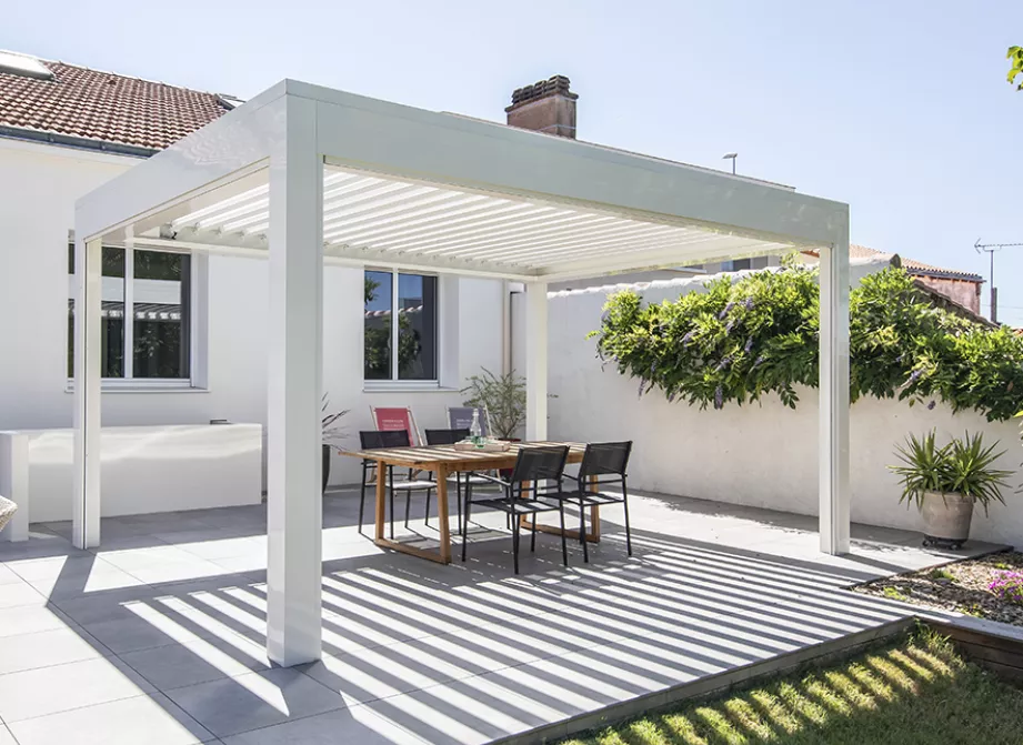 Pergola bioclimatique blanche à lames orientables au-dessus d'une terrasse ensoleillée