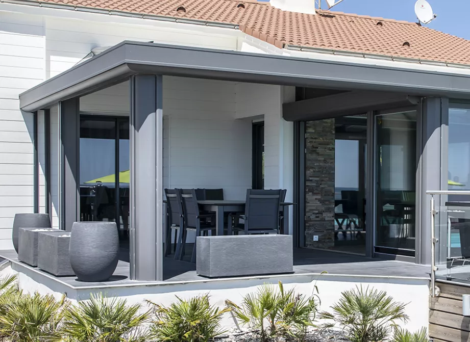 Véranda Soko en aluminium anthracite ouverte sur la mer, posée sur une villa